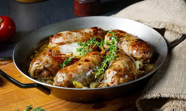 Pieczona biała kiełbasa surowa z cebulą i tymiankiem w metalowej patelni.