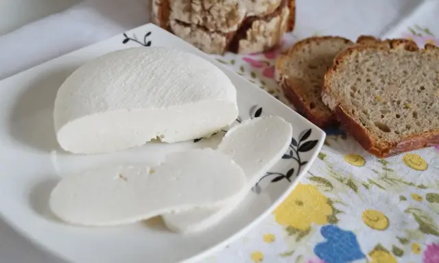 Domowy ser z mleka, pokrojony w plastry, na talerzyku z chlebem. Idealny na śniadanie.