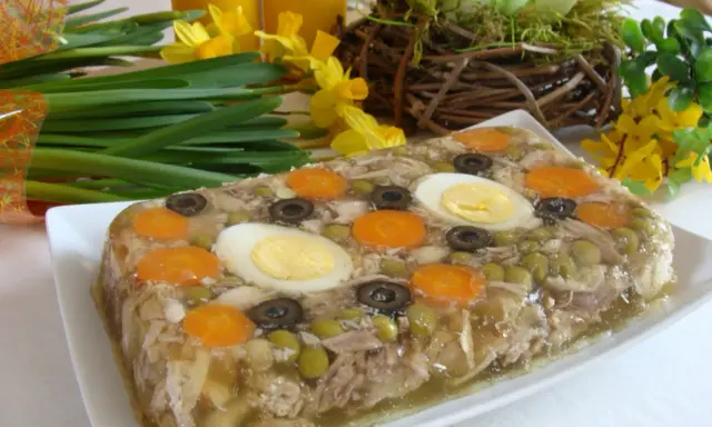 Pyszne nóżki w galarecie z marchewką, jajkiem i oliwkami, ozdobione wiosennymi kwiatami.