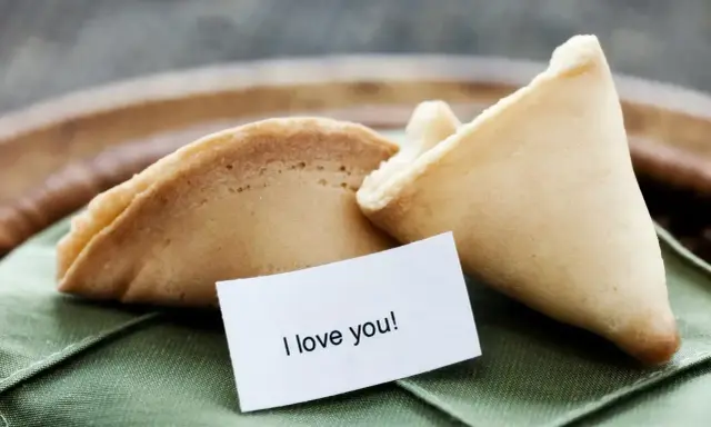 Dwa ciastka z wróżbą na zielonej serwetce. Jedno z nich ma w środku karteczkę z napisem "I love you!".