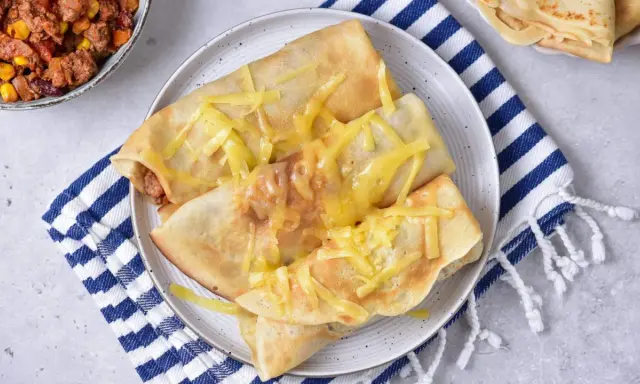 Naleśniki po meksykańsku, zapieczone z serem, obok miseczki z farszem mięsnym i kukurydzą.