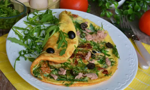 Pyszny omlet z tuńczykiem, rukolą i oliwkami, podany na białym talerzu z żółtym obrusem.