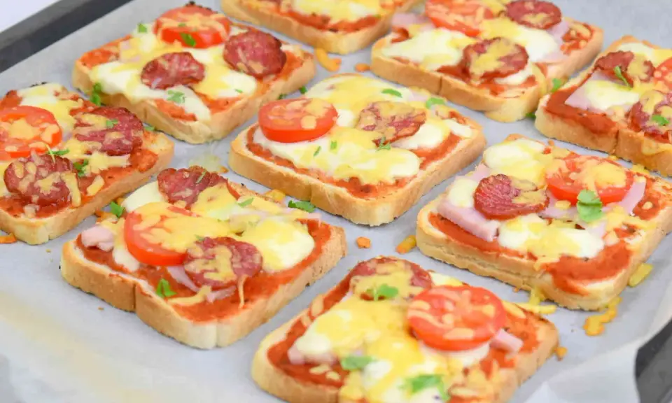 Pyszne, domowe pizza z chleba tostowego z serem, pomidorami i kiełbasą, gotowa do pieczenia.