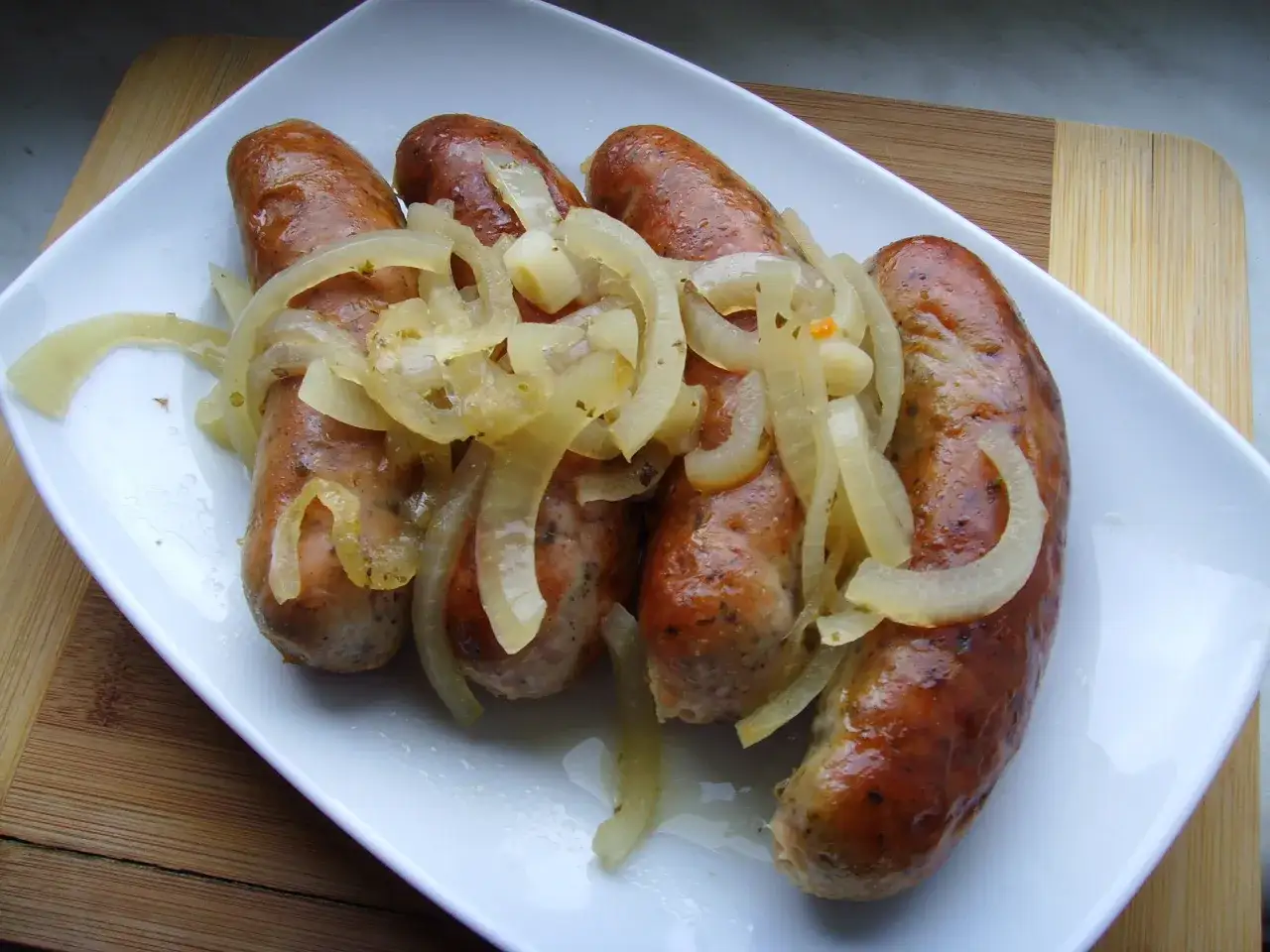 Pieczona biała kiełbasa surowa z cebulą na białym talerzu. Pyszne danie prosto z piekarnika.