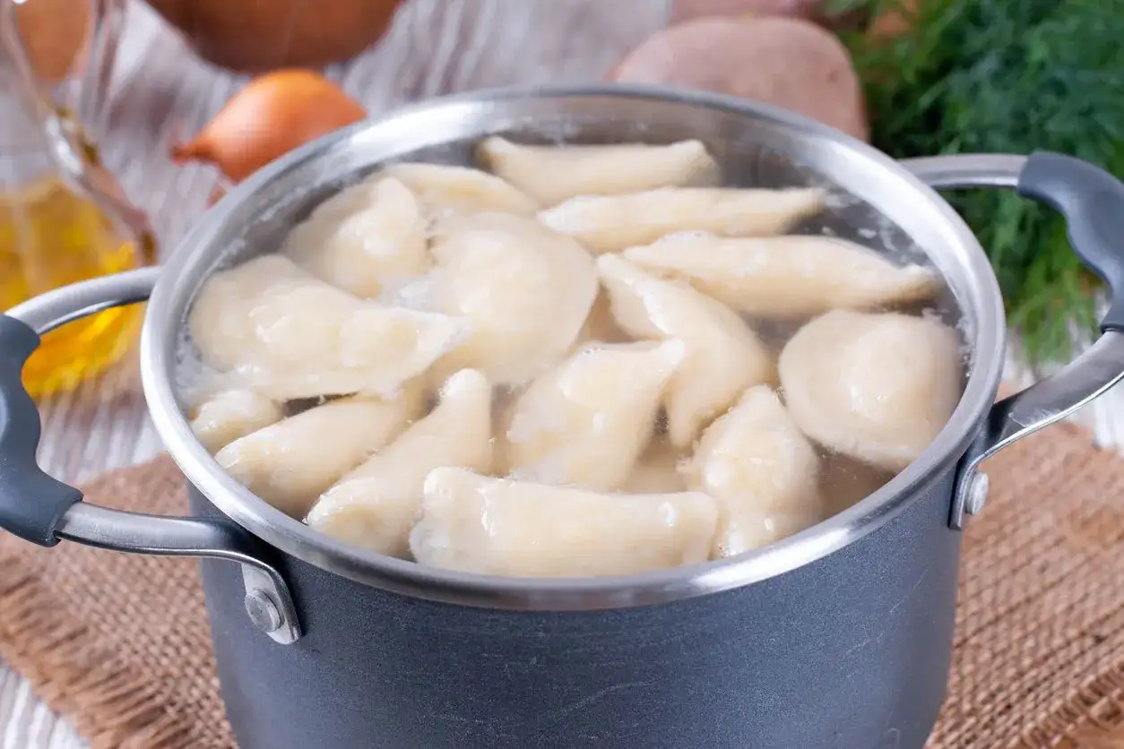 Pierogi gotują się w garnku. Woda wrze, a pierożki wypływają na powierzchnię. Czas, ile gotować pierogi, zależy od ich wielkości i nadzienia.
