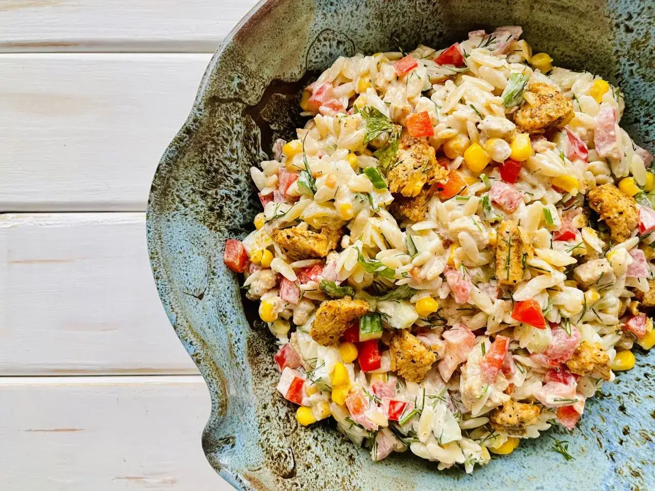 Pyszna sałatka z makaronem orzo, kurczakiem, kukurydzą i papryką, podana w ozdobnej misce.