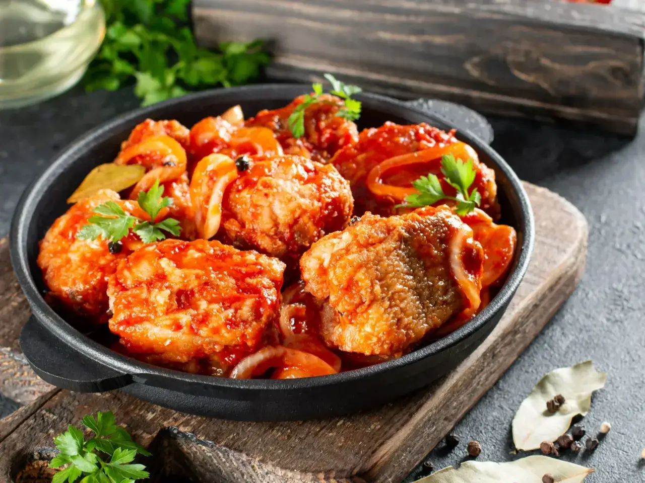 Smażona ryba w sosie pomidorowym z cebulą i natką pietruszki, podana w żeliwnej patelni.