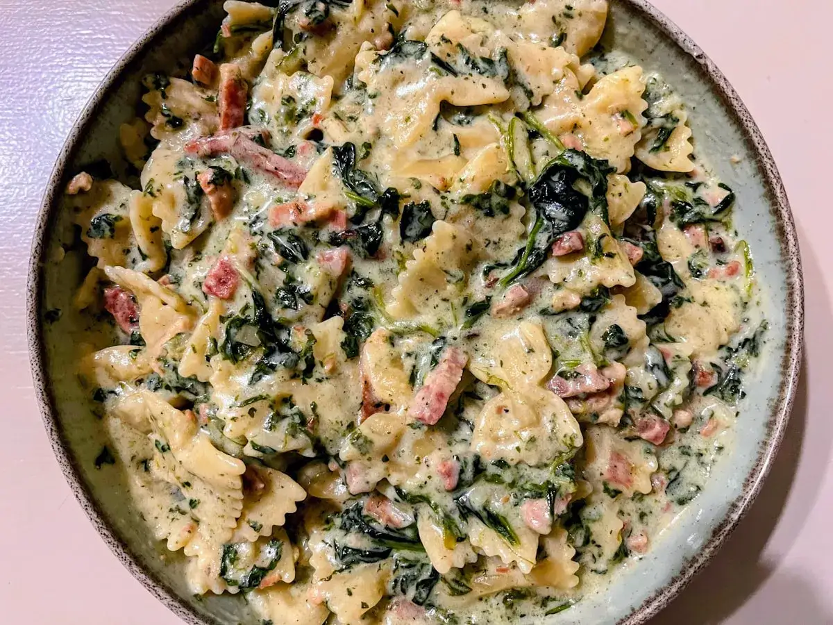 Pyszny makaron farfalle w kremowym sosie ze szpinakiem i kawałkami boczku.