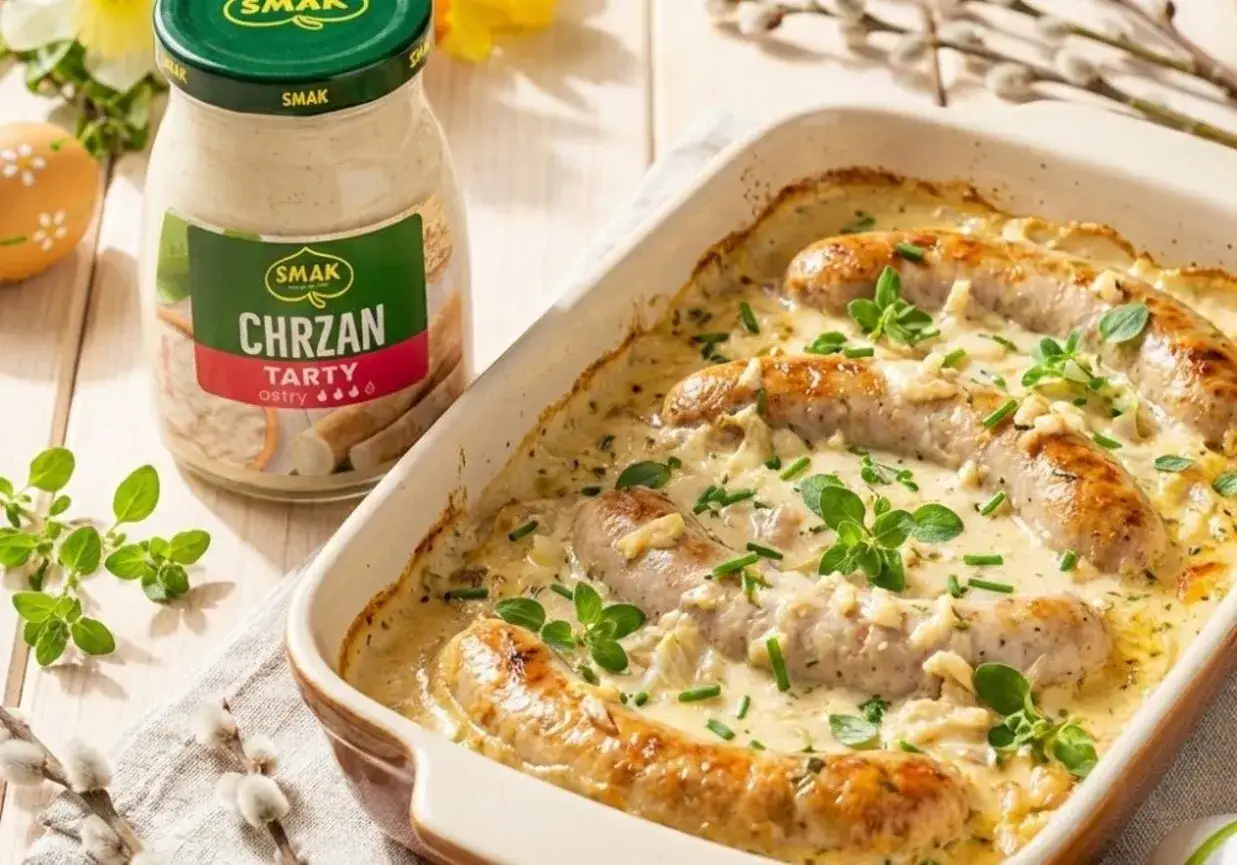 Biała kiełbasa w sosie chrzanowym, zapiekana w naczyniu, obok słoiczek z chrzanem. Idealna na wielkanocny stół.