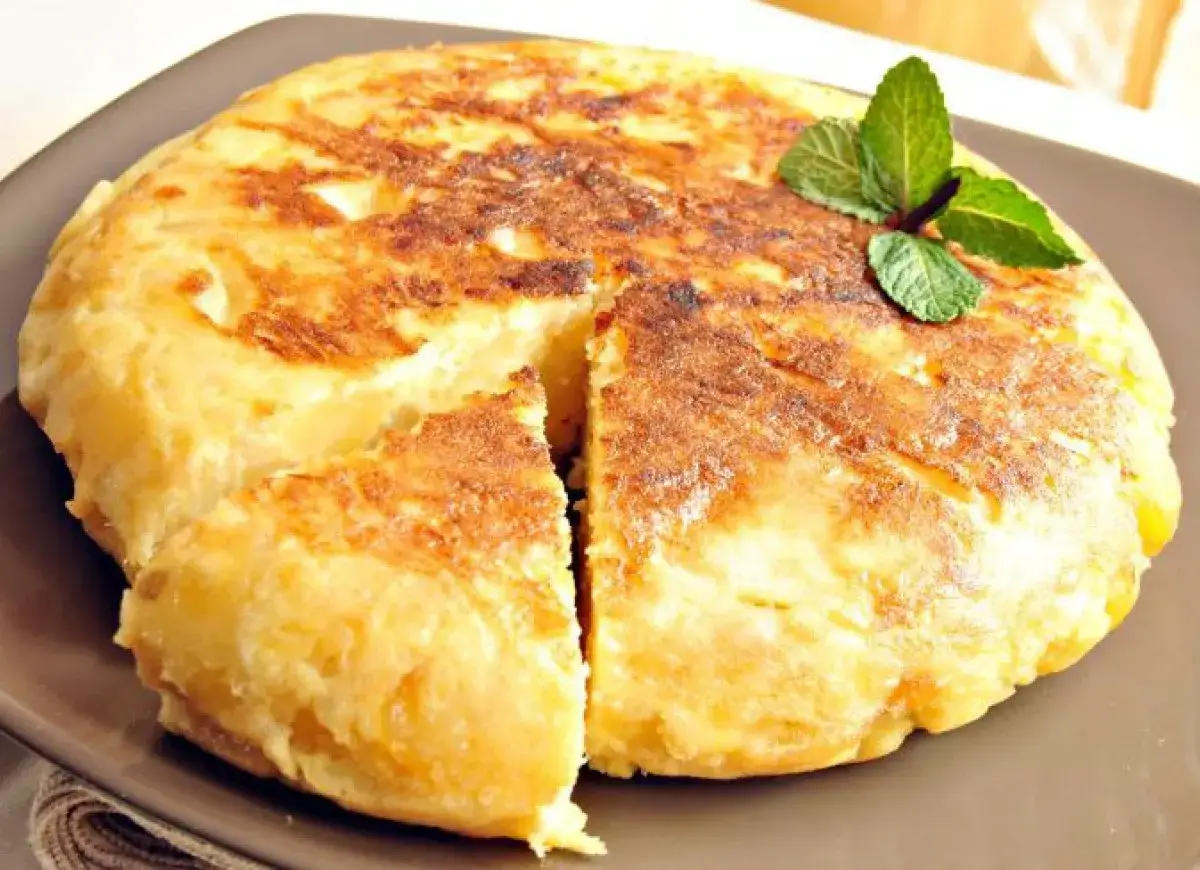 Złocista tortilla de patatas, pokrojona na kawałki, z gałązką mięty. Pyszne danie z ziemniak&oacute;w i jajek.
