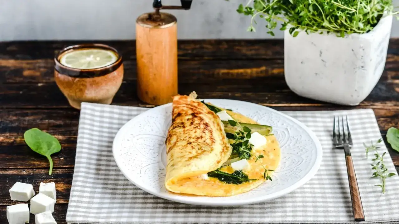 Pyszny omlet ze szpinakiem, serem feta i cukinią, podany na talerzu z ziołami i cytrynową wodą.