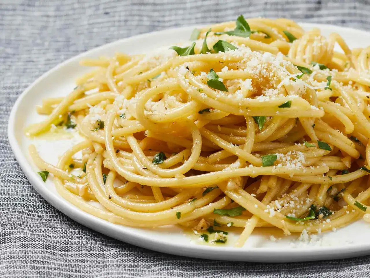 Szybki obiad z makaronem: złociste spaghetti z parmezanem i natką pietruszki, polane oliwą. Pyszne i proste danie.